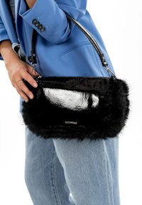 Sac à main en fausse fourrure noire avec un dessus en cuir verni brillant, une quincaillerie argentée et une bandoulière amovible. La texture allie douceur et brillant.
