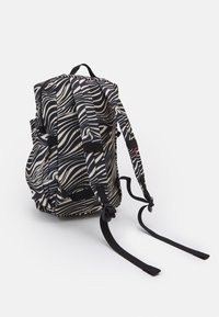 Svart och vit ryggsäck med ett vågigt randmönster, tygremmar och justerbara spännen. Sidor med fickor synliga, strukturerad yta.