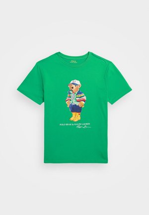 Grünes kurzärmliges T-Shirt mit einem Cartoon-Bären, der eine Mütze, eine gestreifte Jacke, Jeans und gelbe Stiefel trägt, mit dem Text „Polo Bear by Ralph Lauren“ darunter.
