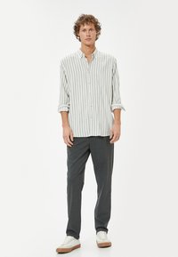 Stribet langærmet skjorte i lys grå og hvid, knappet, sat sammen med mørkegrå bukser og hvide sneakers med beige detaljer.