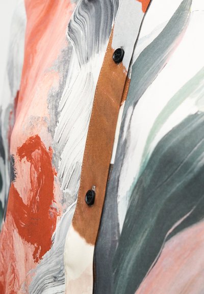 Monivärinen pusero, jossa on abstrakti kuvio oranssin, harmaan ja vihreän sävyissä. Varustettu ruskealla napituslistalla ja mustilla napeilla.