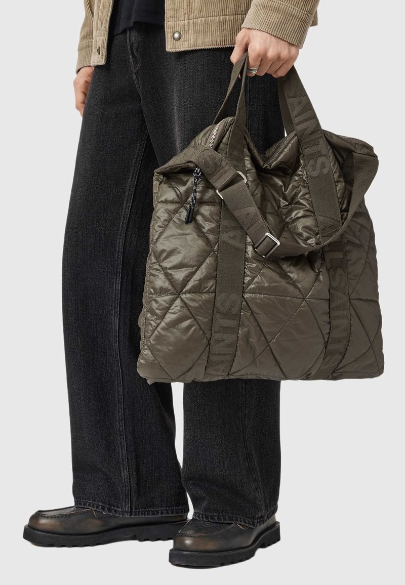 Prošívaná olivově zelená taška na rameno, vybavená zipovým uzávěrem, dvojitými látkovými uchy a potiskem "SAINTS". Texturovaný povrch dodává detail.