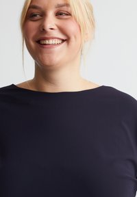 Marineblaues Oberteil mit einem weiten, runden Ausschnitt, glatter Textur und kurzen Ärmeln, das dezente Drapierungen und eine lockere Passform aufweist.
