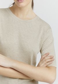 Top a coste beige con maniche corte e scollatura a girocollo. Texture morbida e design aderente, che mette in risalto linee verticali.
