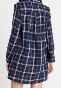 Vestido camisa de cuadros azul marino hecho de tela suave, con mangas largas, puños de botón y un corte relajado. Incluye un detalle de yugo en la parte posterior.