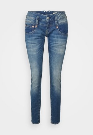 Blå, falmede skinny jeans med forlommer, bæltestropper og knaplukning, vist mod en ens hvid baggrund.