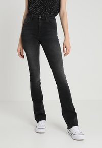 Black denim jeans with a fitted design, mid-rise waist, and standard five-pocket styling, worn with a black polka dot top and white sneakers.
