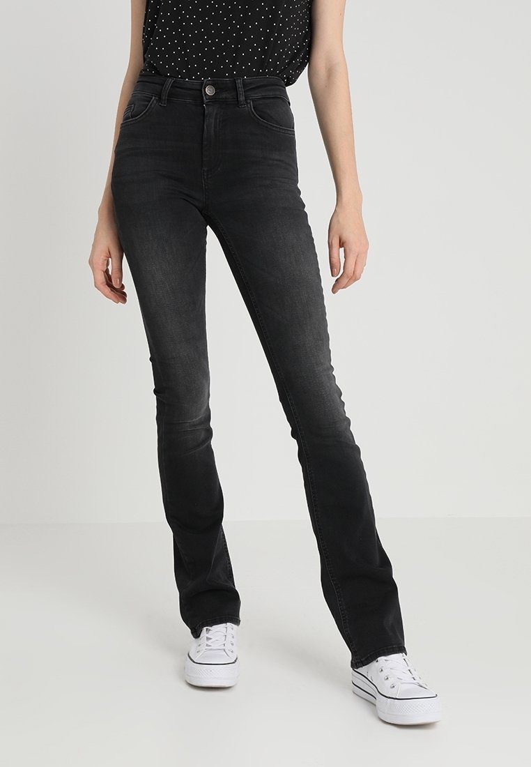 Black denim jeans with a fitted design, mid-rise waist, and standard five-pocket styling, worn with a black polka dot top and white sneakers.