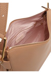 Interno della borsa in pelle beige texturizzata con una fodera rosa pallido, dotato di una tasca con zip e un'etichetta che reca la scritta "Coccinelle."