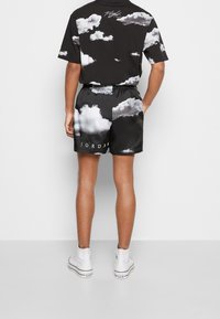 T-shirt noire avec imprimé nuage blanc, assortie à un short noir présentant un imprimé similaire et le texte "JORDAN", porté avec des baskets blanches.