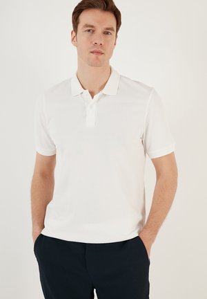 Witte polo met korte mouwen en een klassieke kraag, twee-knopen sluiting en gestructureerde stof. Draagt bij navy broek.