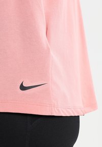 Lyserød kortærmet t-shirt lavet af bomuld, med et sort Nike-logo nederst til venstre. Glat tekstur, afslappet pasform.