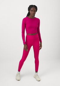Set atletico aderente in un vivace rosa. Crop top a maniche lunghe con design elegante e leggings a vita alta. Tessuto liscio e elasticizzato.