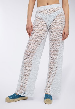 Białe koronkowe spodnie w zygzakowy wzór, z szerokimi nogawkami i elastycznym pasem, połączone z niebieskimi espadrylami.