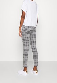 Vit bomull t-shirt, lös passform. Svart och vit rutiga byxor, slim fit med subtil textur. Vita sneakers med guldaccenter.