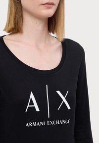 Zwarte langslavende T-shirt met een ruime scoophalshals, met het witte "A|X ARMANI EXCHANGE" logo prominent op de voorkant.