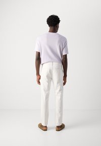 Ljuslila t-shirt med kort ärm i kombination med vita raka byxor och bruna slip-on skor. Enkel, ren design utan synliga mönster.