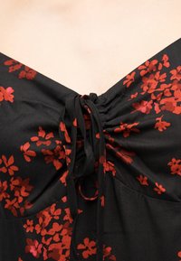 Tissu noir avec un motif floral rouge et un nœud noué au centre de l'encolure d'un vêtement.