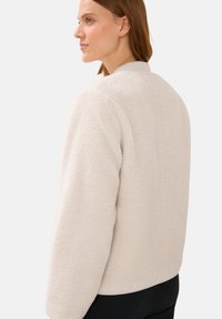 Veste en polaire de couleur écru, avec une texture douce, un col rond et une coupe décontractée. Manches et ourlet côtelés. Vue de dos affichée.