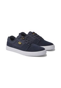 Navy blue suede sneakers with white rubber soles, featuring lace-up design, textured fabric, and a small golden logo on the side.