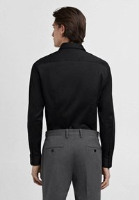 Black long-sleeve shirt with a structured collar and buttoned cuffs, paired with gray tailored trousers featuring two back pockets.