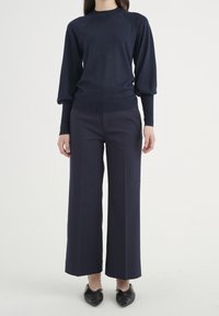 Granatowy dzianinowy pulower z okrągłym dekoltem i bufiastymi rękawami, zestawiony z szerokimi granatowymi spodniami i czarnymi balerinami na spiczastym nosku.