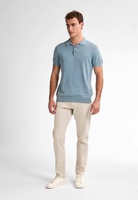 Krátký rukáv polo košile světle modré barvy, vyrobená z měkké látky, s límečkem a třemi knoflíky, doplněná béžovými kalhotami a bílými botami.