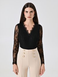 Schwarzer Spitzenbody mit einem gewellten Ausschnitt und langen Ärmeln, kombiniert mit hoch-taillierten beigen Hosen mit goldenen Knopfdetails.