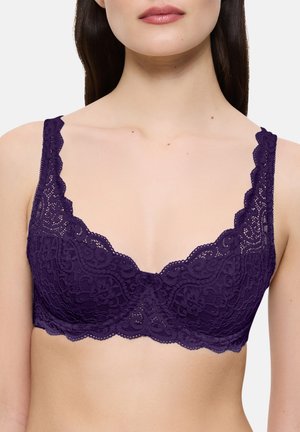 Femme portant un soutien-gorge en dentelle violet profond avec des bords festonnés et des motifs floraux complexes sur les bonnets et les bretelles.