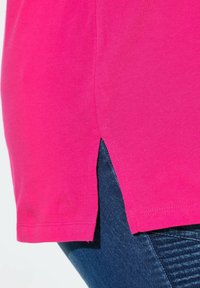 Rosa Kurzarm-T-Shirt mit seitlichen Schlitzen am Saum, aus weichem Stoff, kombiniert mit dunkelblauen strukturierten Jeans.