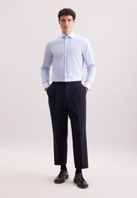 Blauw-wit gestreepte overhemd met lange mouwen, gecombineerd met donkerblauwe geplooide broek en zwarte lederen schoenen.