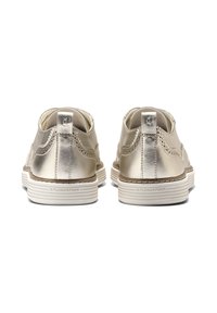 Un paio di scarpe lacciate in metallo dorato viste da dietro, con suole bianche imbottite etichettate 'FLOWERFOAM' e cuciture decorative.