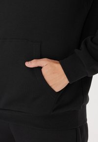 Käsi le resting musta pikka varrukaga sviiterid, millel on soonikuga mansetid ja serv.