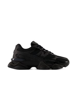 Scarpa da ginnastica nera con suola spessa, tomaia in mesh e pelle e logo laterale, mostrata dal lato esterno su sfondo bianco.