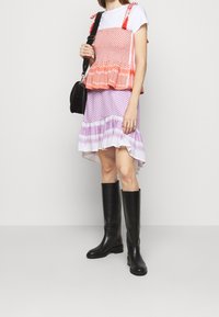 Layered dress with an orange patterned top, flowing purple skirt, and high black leather boots. Features ruffled hems and shoulder tassels.