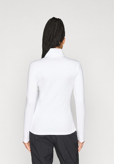 Λευκή μακρυμάνικη μπλούζα με ψηλό γιακά, λεία υφή, εφαρμοστή γραμμή και ελάχιστες ραφές, συνδυασμένη με μαύρο παντελόνι.