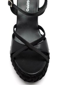 Sandalia negra con textura trenzada en la suela, tiras entrecruzadas de cuero suave y diseño de tacón plano.