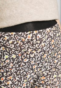 Leggings negros con cintura elástica que presentan un material texturizado con un patrón abstracto multicolor en tonos de amarillo, naranja y blanco.
