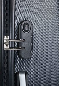 Detalle de una maleta rígida negra con superficie texturizada, cremallera metálica y mecanismo de cierre negro con dos palancas plateadas.