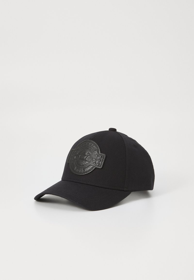 Casquette de baseball noire en tissu, avec un patch en cuir noir texturé à l'avant comportant un motif circulaire en relief.