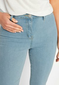 Ljusblå högmidjade jeans i denim, med slim fit, framfickor och synlig sömnad vid midjan och gylfen.