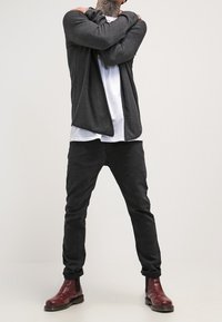 Tmavě šedý cardigan přes bílé tričko, doplněný černými slim-fit kalhotami a vínovými kotníkovými botami. Vyznačuje se volným střihem a čistými liniemi.