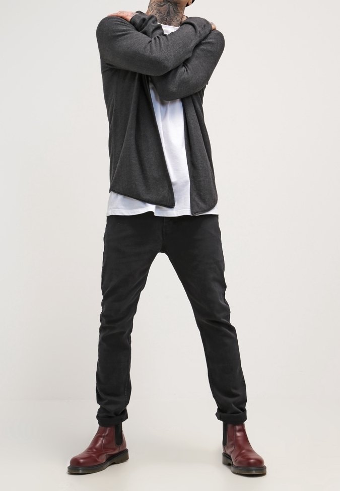 Tmavě šedý cardigan přes bílé tričko, doplněný černými slim-fit kalhotami a vínovými kotníkovými botami. Vyznačuje se volným střihem a čistými liniemi.