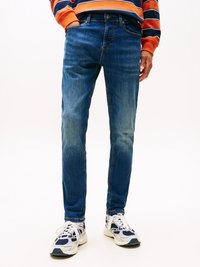 Jeans de denim azul ajustados con una textura desgastada, diseño de cinco bolsillos y detalles de costura, combinados con zapatillas blancas y marinas.