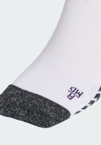 Valkoinen nilkkasukka, jossa musta vahvistettu kärki ja pieni violetti logo lähellä kärkialuetta vaalealla taustalla.