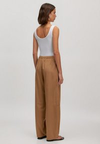 Witte mouwloze top gecombineerd met lichtbruine wijde broek, met een gladde textuur en een elastische tailleband. Zwarte platte sandalen inbegrepen.