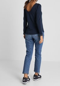 Marineblauwe blouse met stippen, een V-hals en pofmouwen, gecombineerd met lichtblauwe jeans en zwarte sneakers met witte accenten.