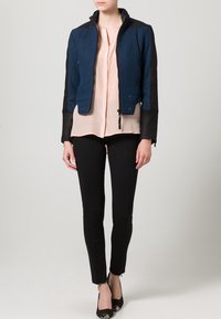 Blå och svart kort jacka med dragkedja fram, texturerad tyg och släta läderärmar, lagd över en ljusrosa skjorta och svarta byxor.