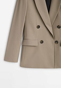 Veste beige croisée à quatre boutons foncés, revers crantés, manches longues et poches à rabat fendu de chaque côté.