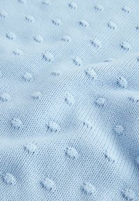 Svetlomodrá pletená tkanina s vystúpeným vzorom bobľových stehů vytvárajúca textúrovaný bodkovaný povrch.